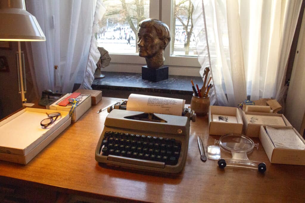 Astrid Lindgrenin kirjoituspöytä, jossa kirjoituskone, suurennuslasi ja patsas ikkunalaudalla